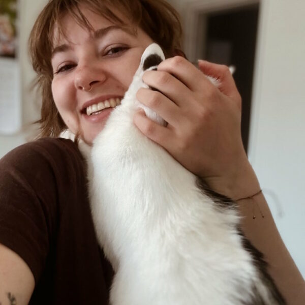 Uśmiechnięta kobieta przytulająca się z białym kotem w czarne łatki. Kompleksowa i czuła opieka dla kotów z różnymi potrzebami. Petsitter Kraków