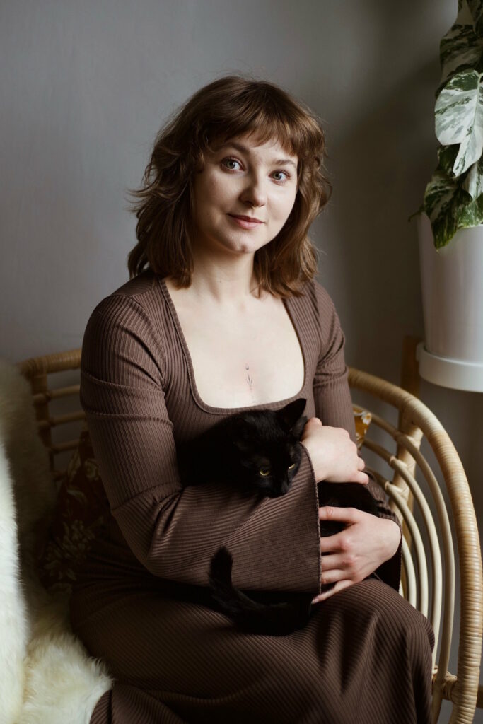 Kobieta w brązowej sukience siedzi na fotelu trzymając na kolanach czarnego kota. Nawiąż kontakt z Izabelą Stańczyk – psycholożką i kocią specjalistką.