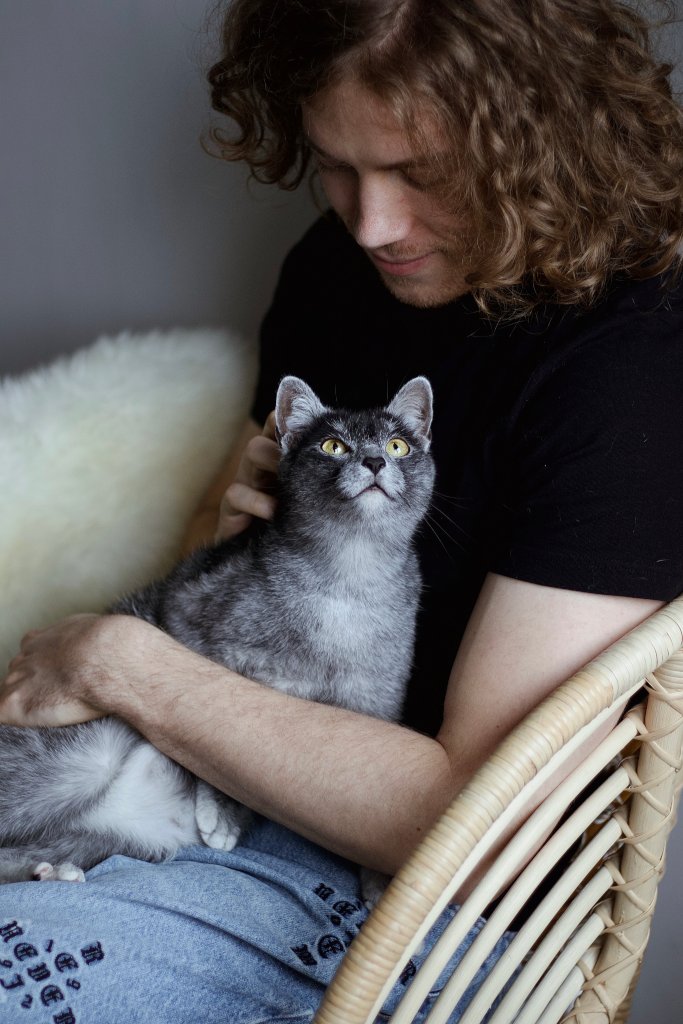 Mężczyzna relaksujący się w towarzystwie szarego kota. Felinoterapia pomaga w redukcji stresu i budowaniu głębokiej więzi między kotem a człowiekiem.
