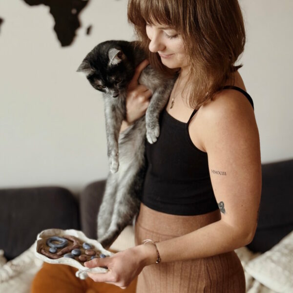 Specjalista diety BARF dla kota trzymająca na rękach kotkę w kolorze karpati oraz ceramiczną miseczkę spowalniającą jedzenie.